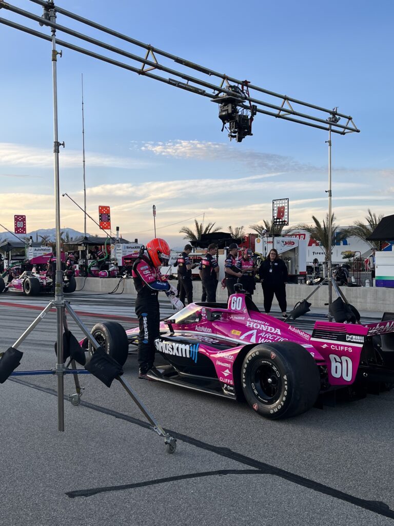 Professional film crew filming an IndyCar race car with a technocrane, demonstrating high-end service production logistics and technical capabilities.